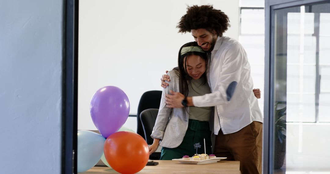 Multiracial Coworkers Hugging and Celebrating with Cupcakes and Balloons in Modern Office