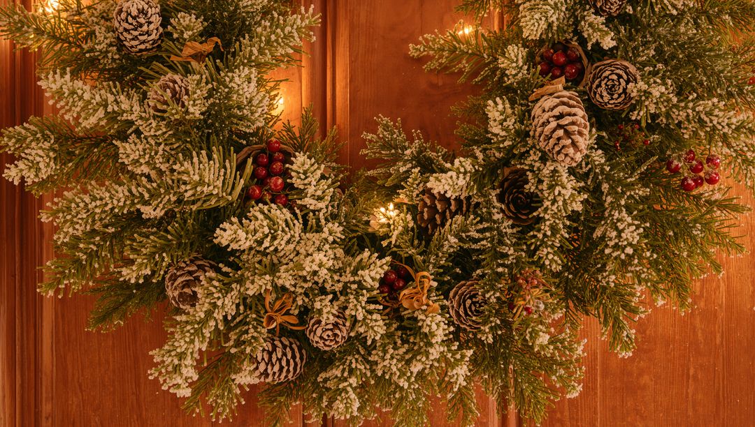 Hanging Flocked Evergreen Wreath with Pine Cones Red Berries Warm Lights on Wood Door