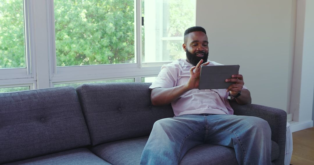 Man Relaxing on Couch Using Tablet with Earbuds in Bright Living Room