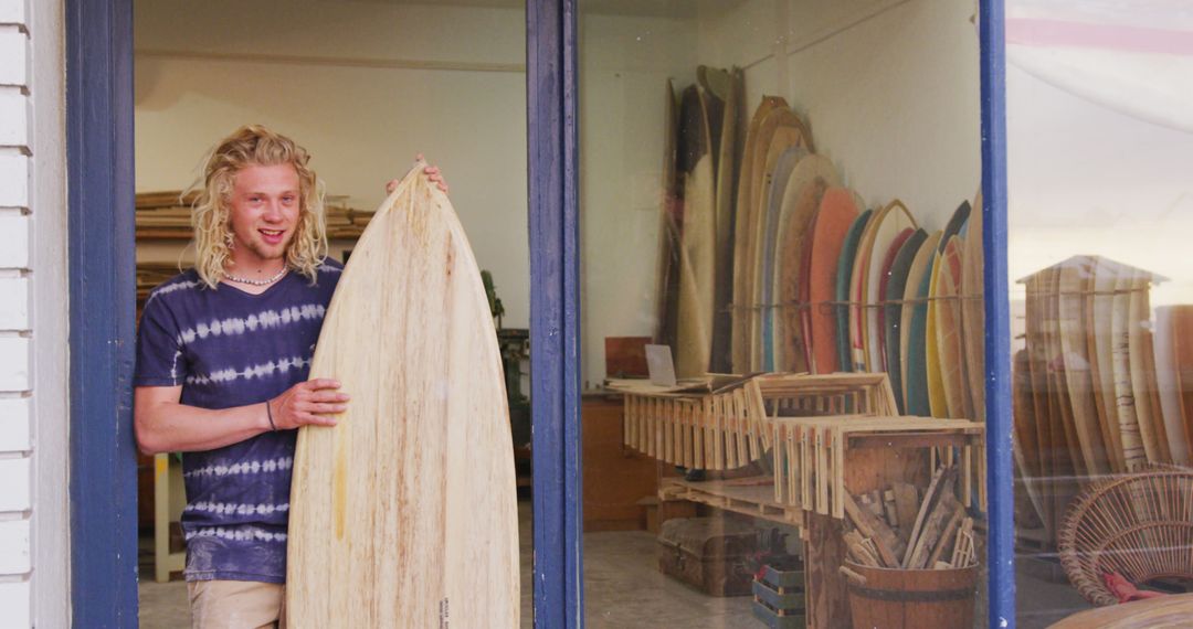 Young Surfer Holding Wooden Surfboard Outside Shop with Multiple Surfboards - Free Images, Stock Photos and Pictures on Pikwizard.com