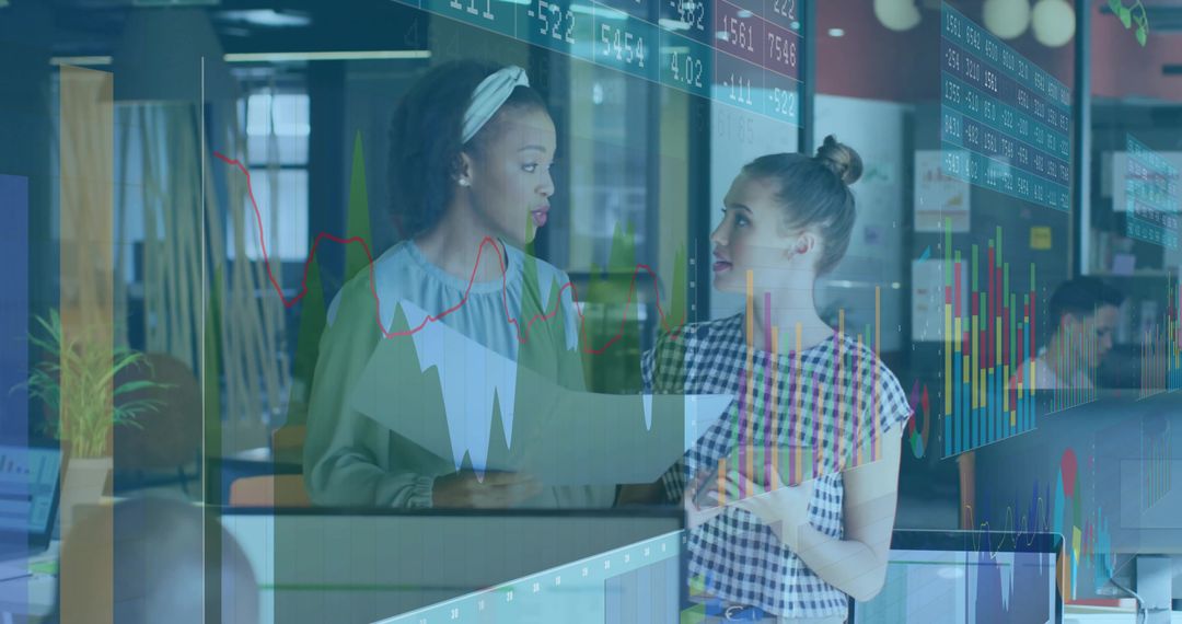 Collaborating women analyzing market charts through glass partition in modern open office