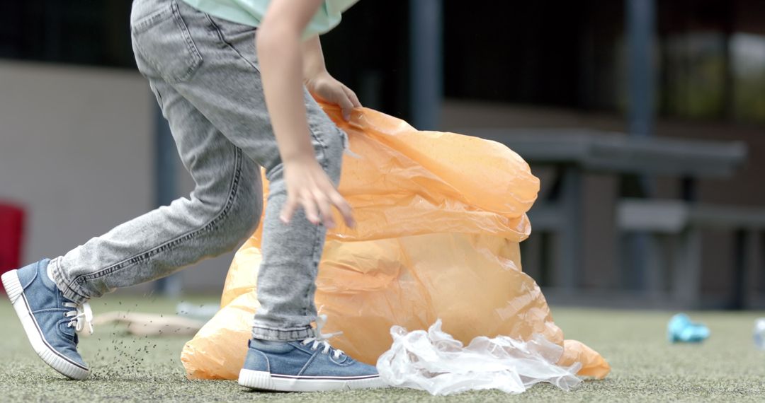 Child Picking Up Trash with Large Orange Bag in Playground