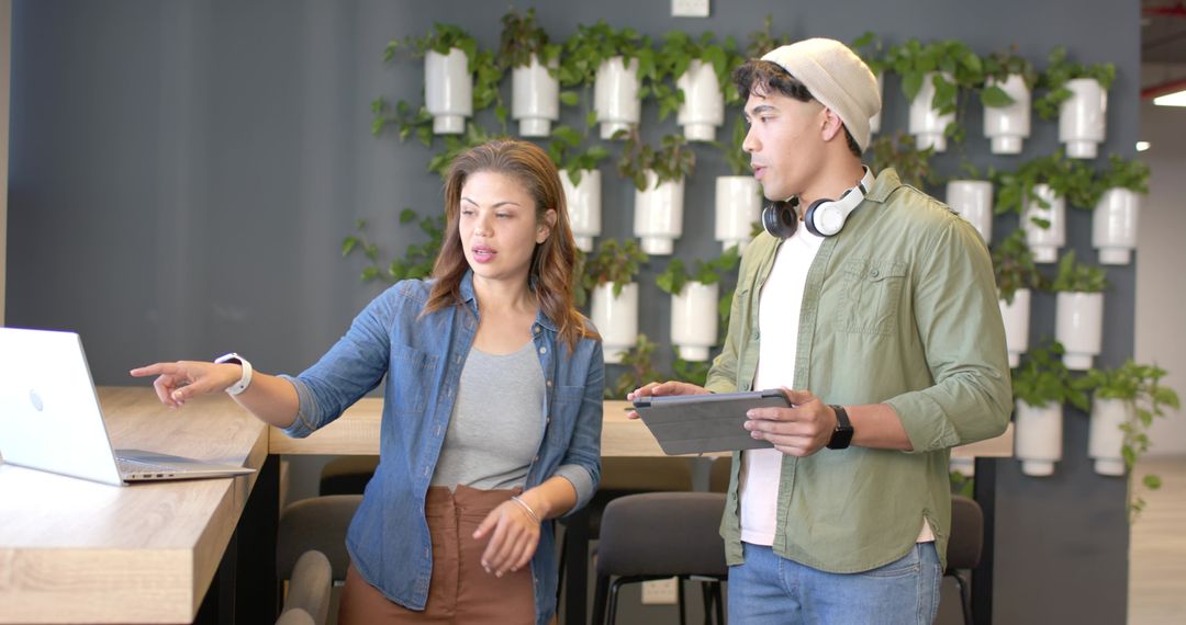 Coworkers pointing at laptop and collaborating with tablet in modern coworking space