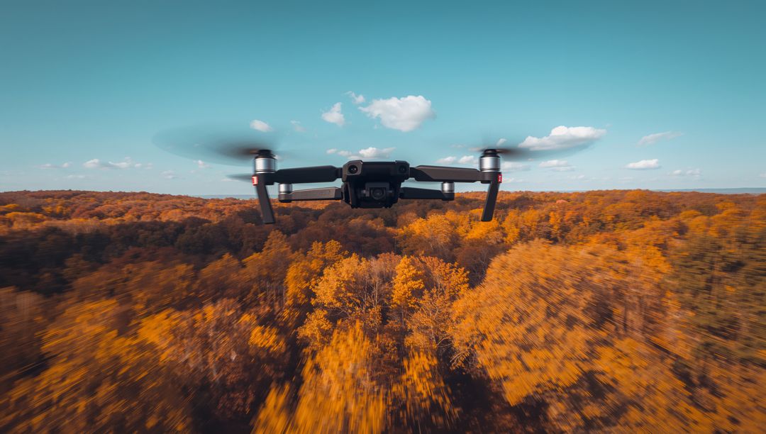 Flying quadcopter drone hovering over autumn forest with gimbal camera and motion blur