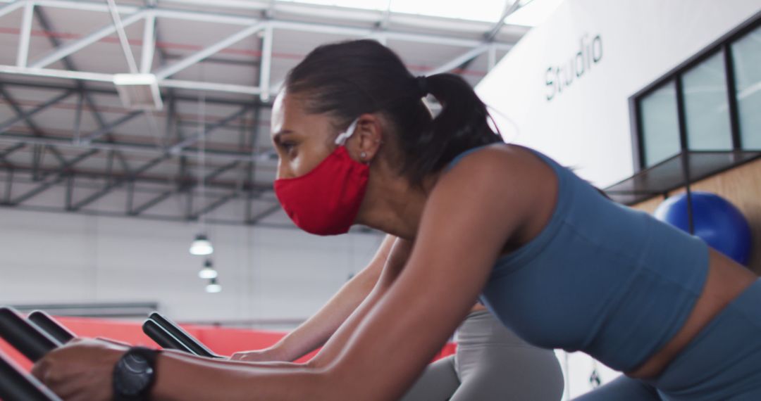 Woman Wearing Red Mask Exercising on Stationary Bike in Modern Gym - Free Images, Stock Photos and Pictures on Pikwizard.com