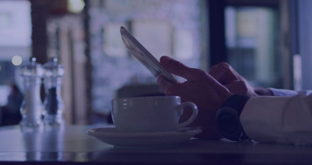 Tapping smartphone at cafe table with coffee cup and smartwatch for mobile productivity