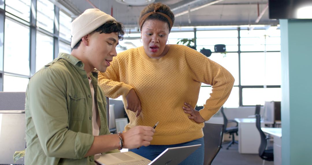 Multicultural colleagues collaborating over laptop with surprised reaction in modern open office