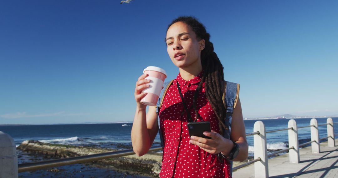 Young Woman Drinking Coffee by the Ocean While Using Smartphone - Free Images, Stock Photos and Pictures on Pikwizard.com