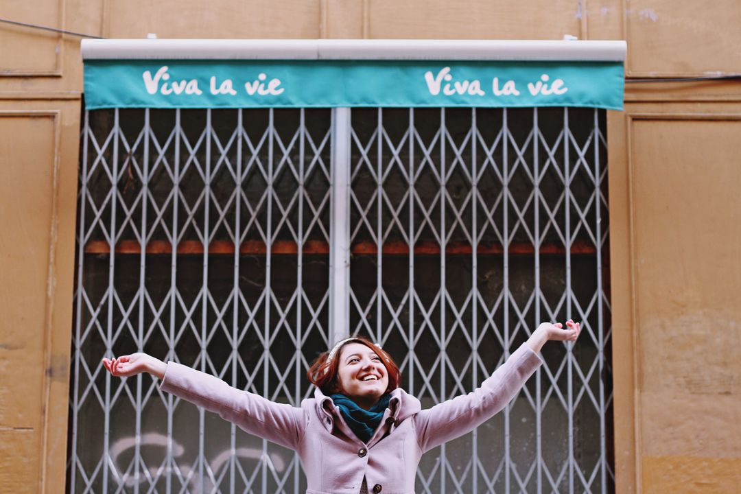 Joyful Young Woman Celebrating in Front of Store with Viva La Vie Sign - Free Images, Stock Photos and Pictures on Pikwizard.com