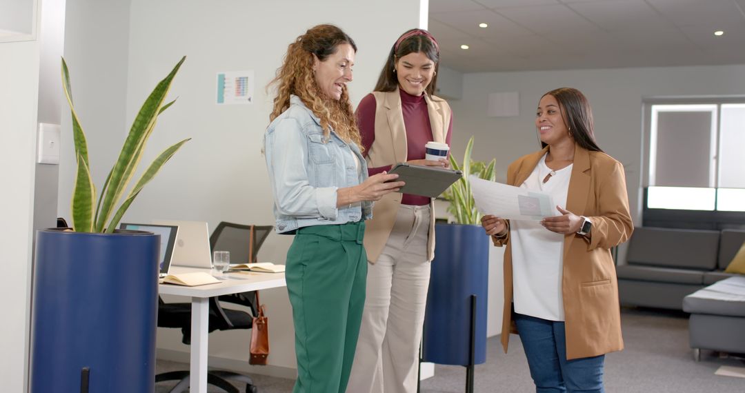 Diverse female colleagues collaborating with tablet and documents in modern office
