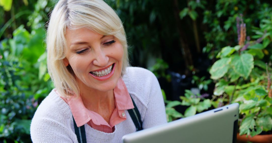 Smiling Mature Woman Using Tablet in Outdoor Garden - Free Images, Stock Photos and Pictures on Pikwizard.com