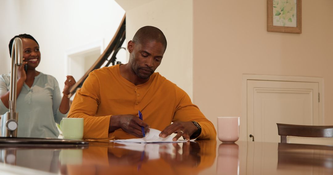 Man Reviewing Documents at Home Kitchen Table with Coffee Mugs