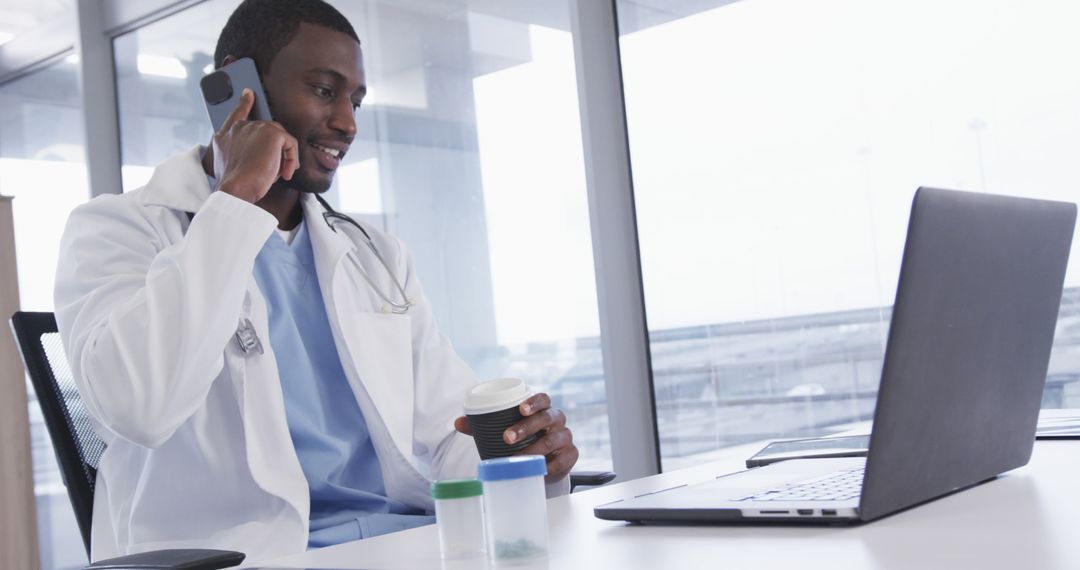 Doctor Holding Coffee Cup Talking on Phone and Using Laptop in Office - Free Images, Stock Photos and Pictures on Pikwizard.com