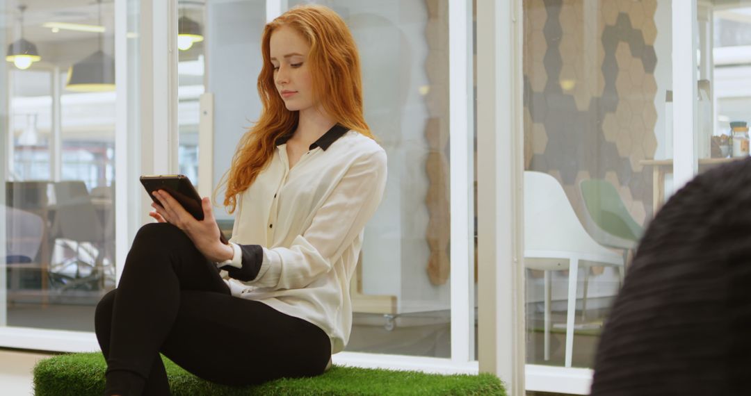 Young Caucasian woman sits absorbed in her tablet at the office - Free Images, Stock Photos and Pictures on Pikwizard.com