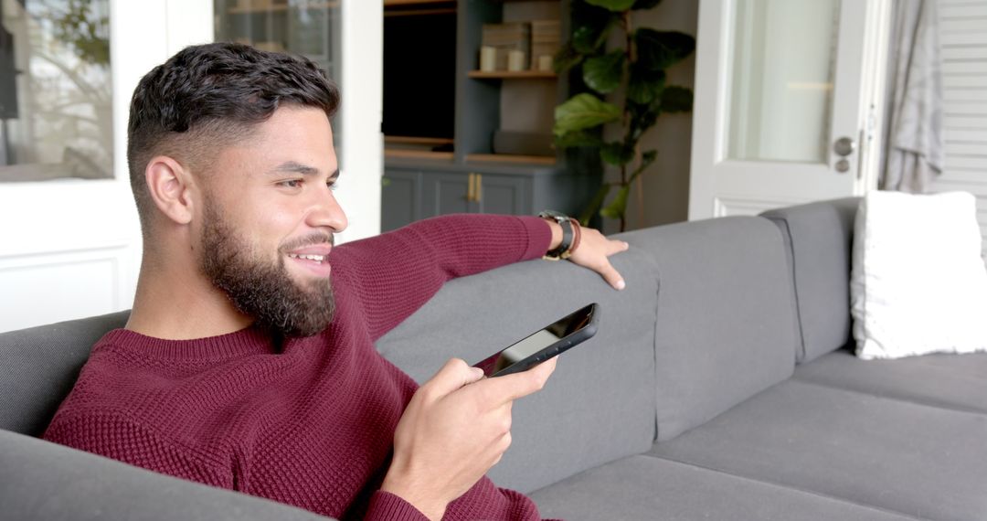Happy Man Relaxing on Sofa with Smartphone in Hand