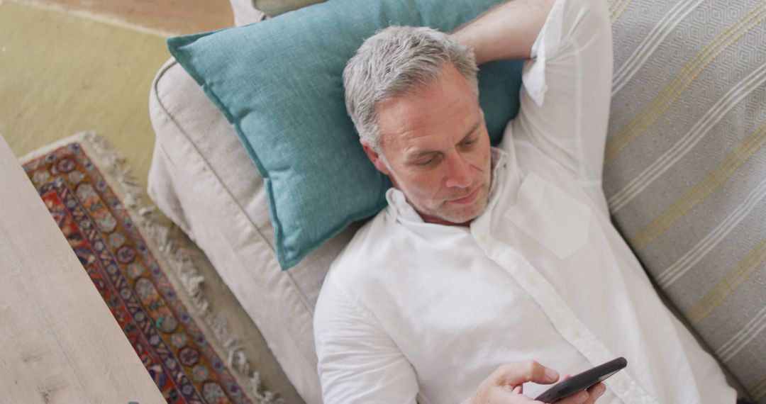 Middle-aged man relaxing on couch while using smartphone - Free Images, Stock Photos and Pictures on Pikwizard.com