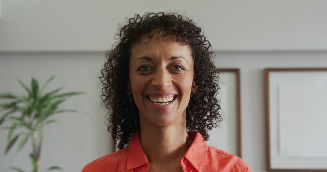 Smiling Woman with Curly Hair in Orange Shirt in Home Setting - Free Images, Stock Photos and Pictures on Pikwizard.com