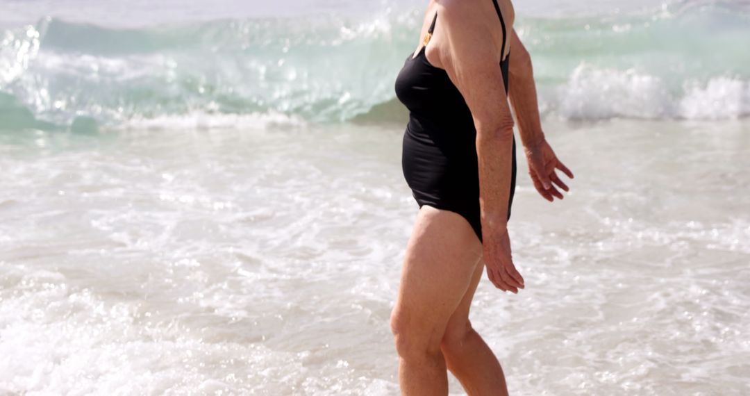 Senior Woman Walking Along Beach Shore in Swimsuit - Free Images, Stock Photos and Pictures on Pikwizard.com