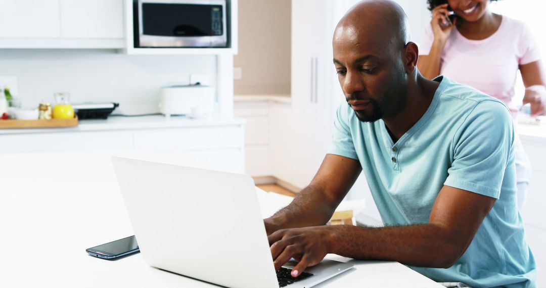 Man Working on Laptop in Kitchen While Woman Talking on Phone - Free Images, Stock Photos and Pictures on Pikwizard.com