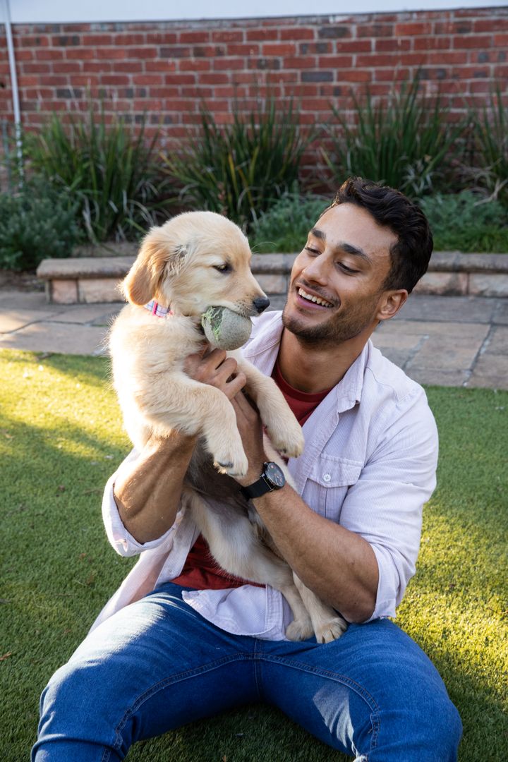 Happy Man Playing with Golden Retriever Puppy Outdoors