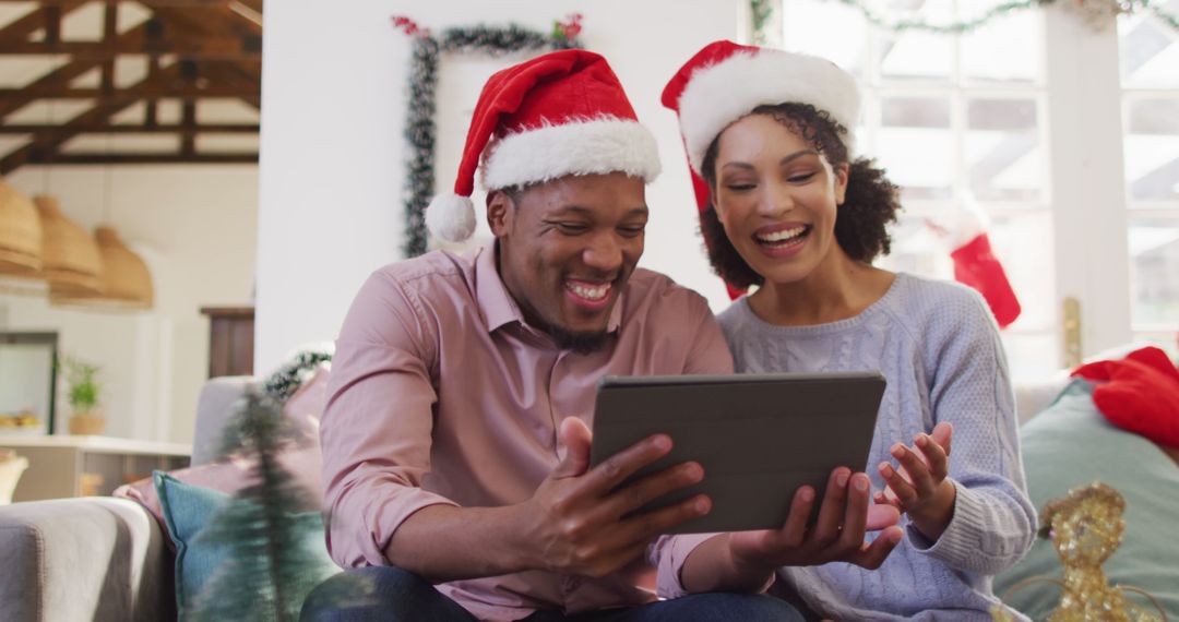 Happy couple wearing Santa hats using tablet on cozy Christmas morning - Free Images, Stock Photos and Pictures on Pikwizard.com