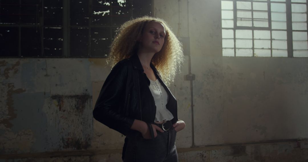 Confident Young Woman with Curly Hair Standing in Abandoned Warehouse - Free Images, Stock Photos and Pictures on Pikwizard.com