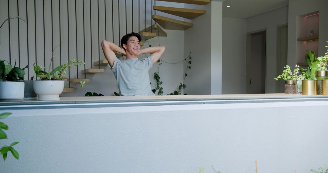 Asian Man Relaxing on Modern Balcony with Greenery
