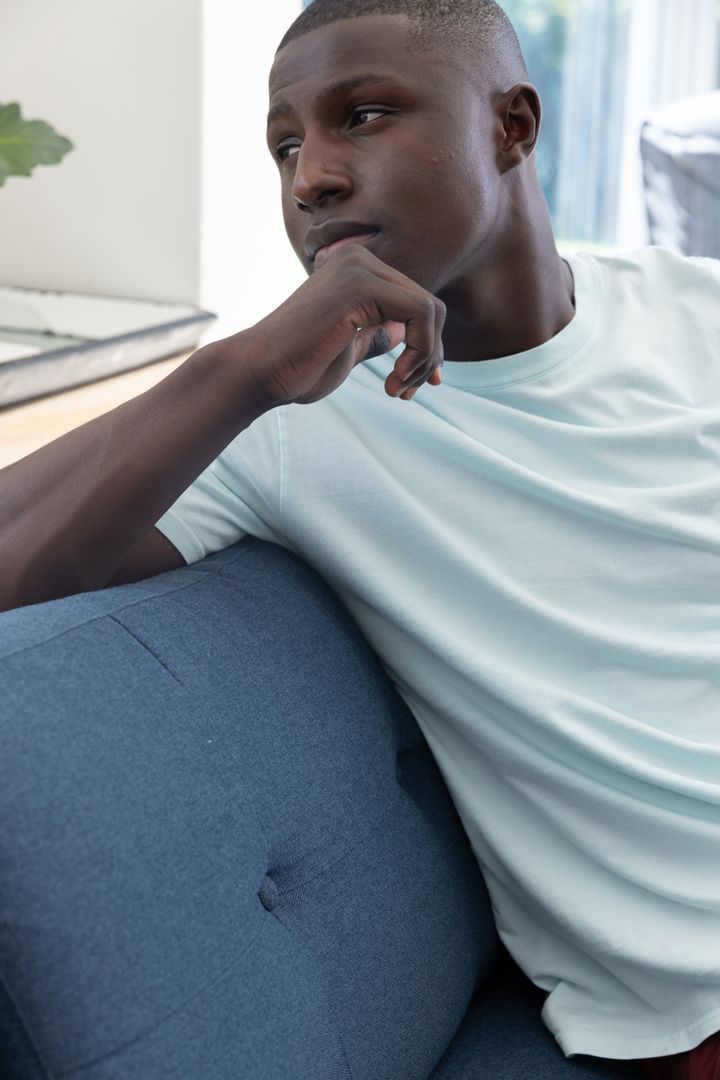 Man in Teal Shirt Relaxing on Blue Couch by Window at Home