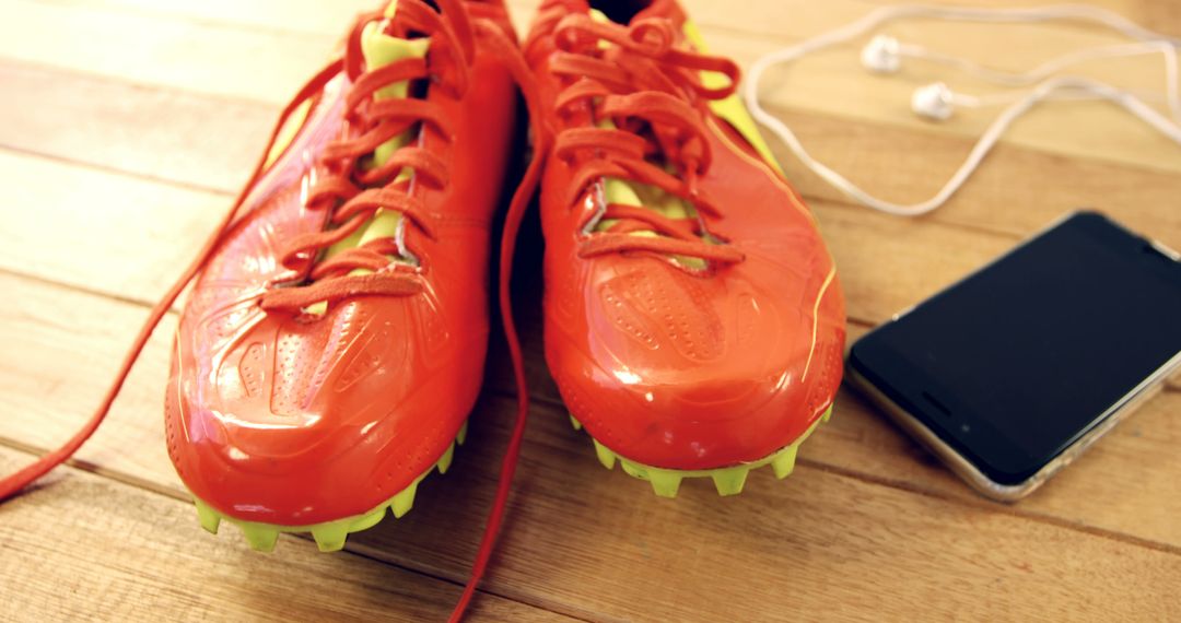 Vibrant orange soccer cleats with smartphone on wooden floor - Free Images, Stock Photos and Pictures on Pikwizard.com