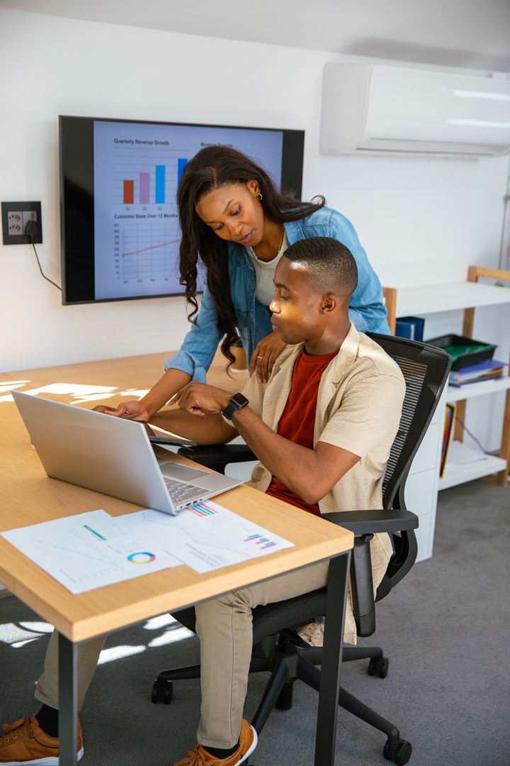Coworkers Analyzing Business Data on Laptop in Modern Office Environment