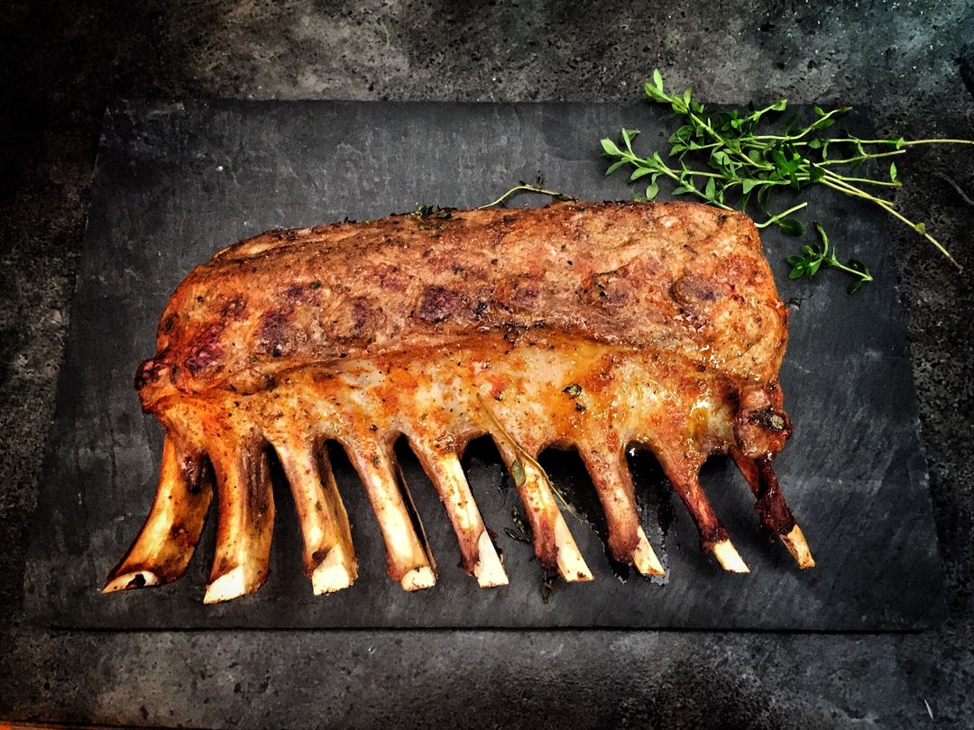 Roasting rack of lamb on slate board with thyme garnish and charred bones
