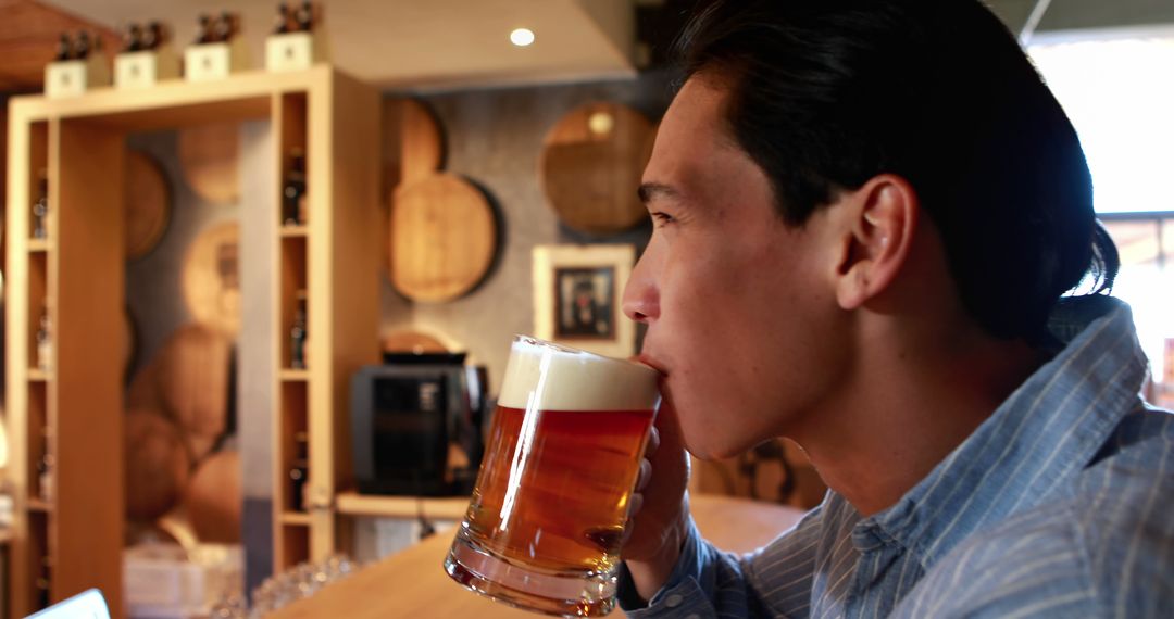 Asian Man Drinking Beer in Cozy Pub with Relaxed Atmosphere
