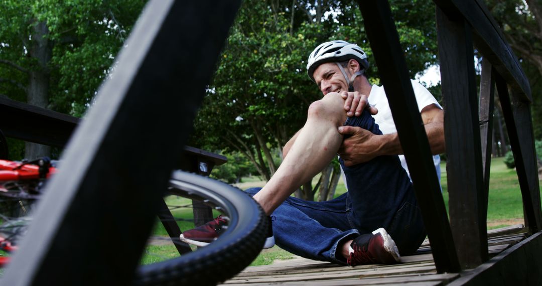 Injured Cyclist Holding Knee on Wooden Bridge in Park - Free Images, Stock Photos and Pictures on Pikwizard.com