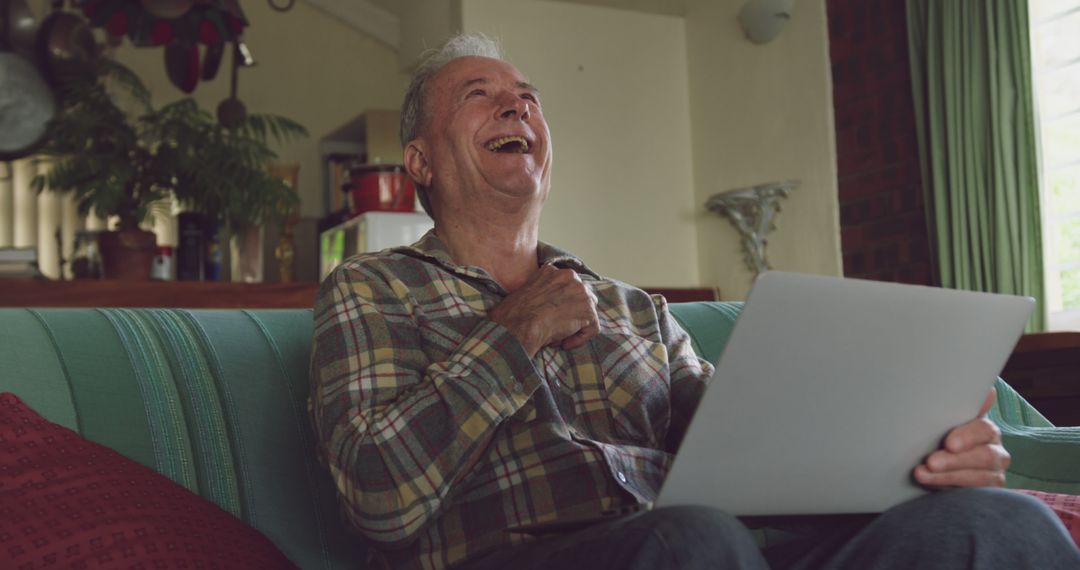 Elderly Man Laughing While Using Laptop on Couch - Free Images, Stock Photos and Pictures on Pikwizard.com