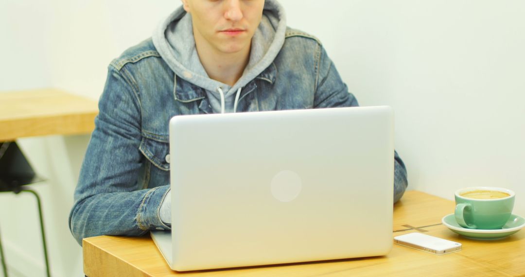 Young Man in Denim Jacket Working on Laptop at Minimalist Cafe - Free Images, Stock Photos and Pictures on Pikwizard.com