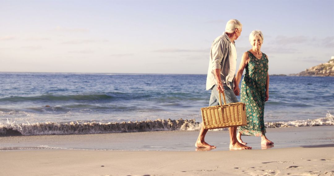 Happy Senior Couple Walking on Beach Holding Picnic Basket - Free Images, Stock Photos and Pictures on Pikwizard.com