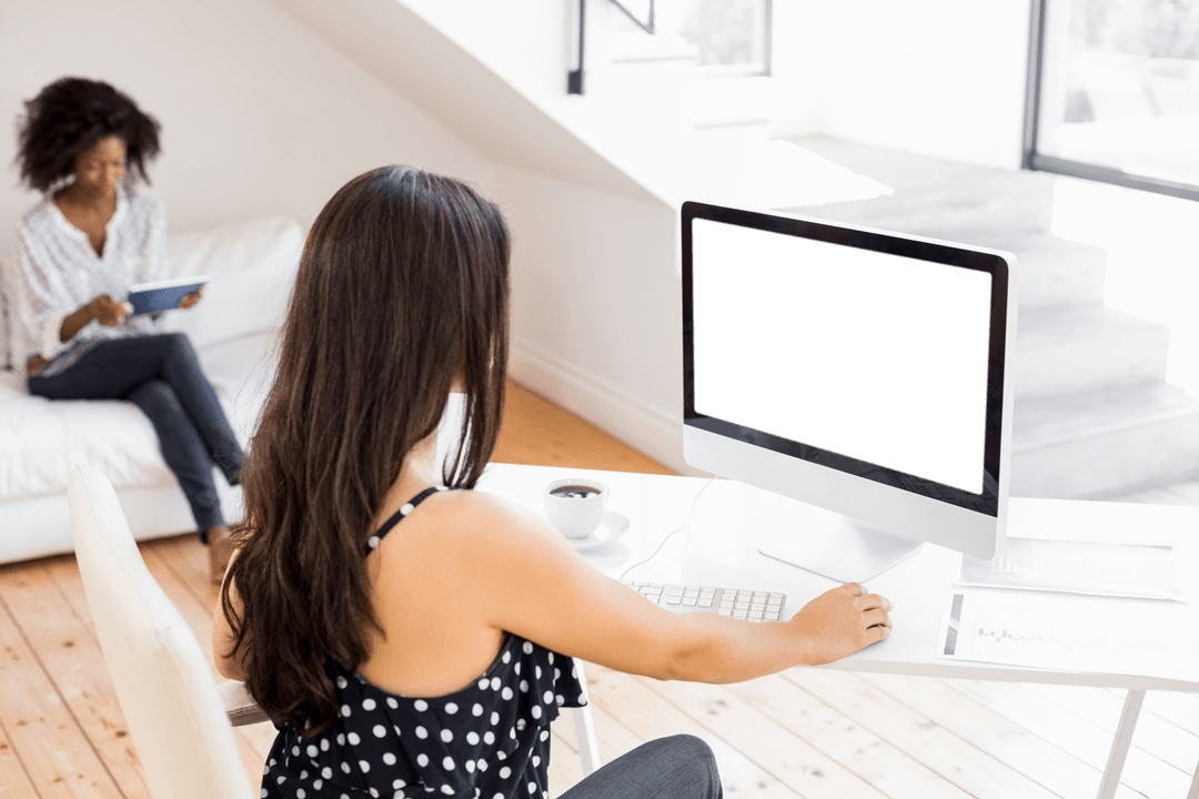 Asian Woman at Desk Using Desktop with Coffee and Tablet User in Background