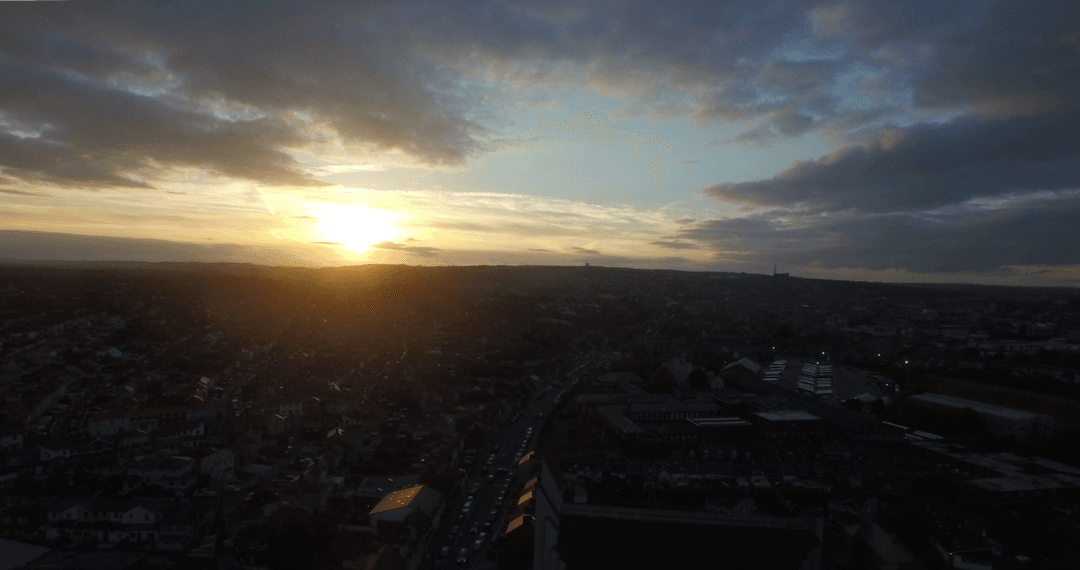 Transparent sunset over urban silhouette against cloudy sky