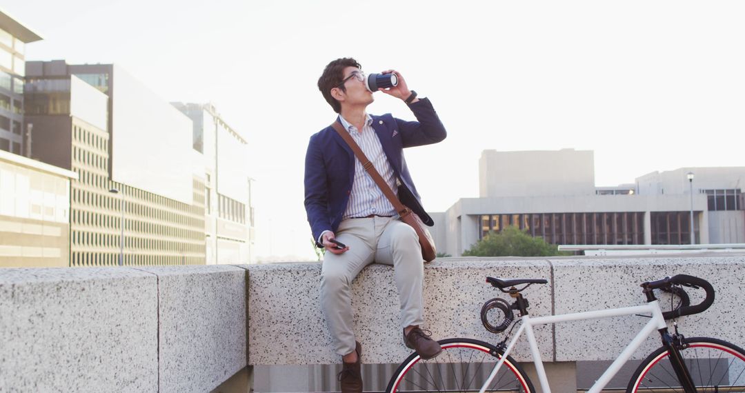 Asian man drinking coffee and using smartphone while sitting on the roof of corporate park - Free Images, Stock Photos and Pictures on Pikwizard.com