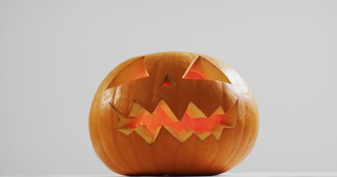 Glowing Jack-o-Lantern with Jagged Teeth Sitting on Minimal White Surface for Halloween