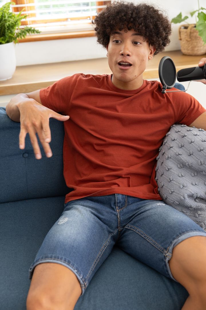 Curly-haired Man Recording Podcast at Home on Sofa