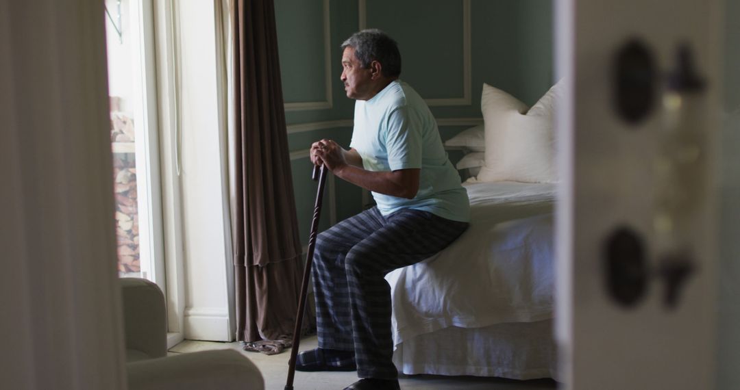 Senior Man Sitting on Bed with Cane by Window in Bedroom - Free Images, Stock Photos and Pictures on Pikwizard.com