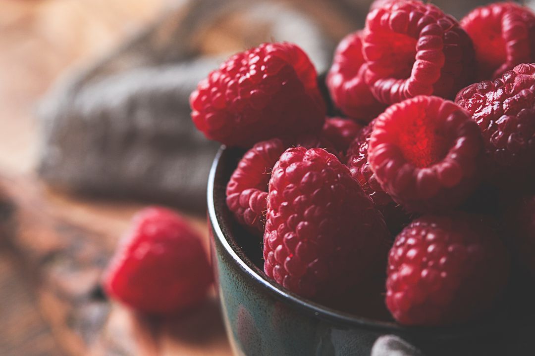 Close-up ripe raspberries in ceramic bowl on rustic wooden table, shallow depth of field