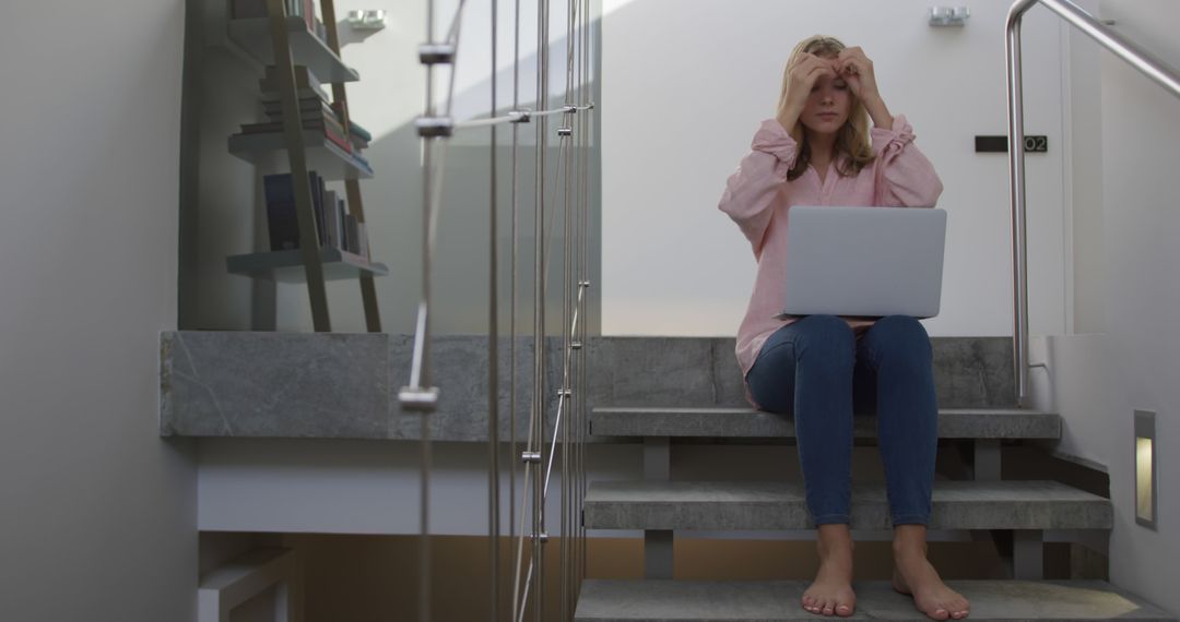 Stressed Woman Sitting on Stairs Holding Head While Using Laptop - Free Images, Stock Photos and Pictures on Pikwizard.com