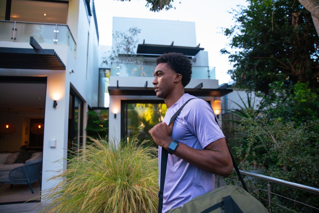 Man Checking Smartwatch Outside Modern Home with Duffle Bag