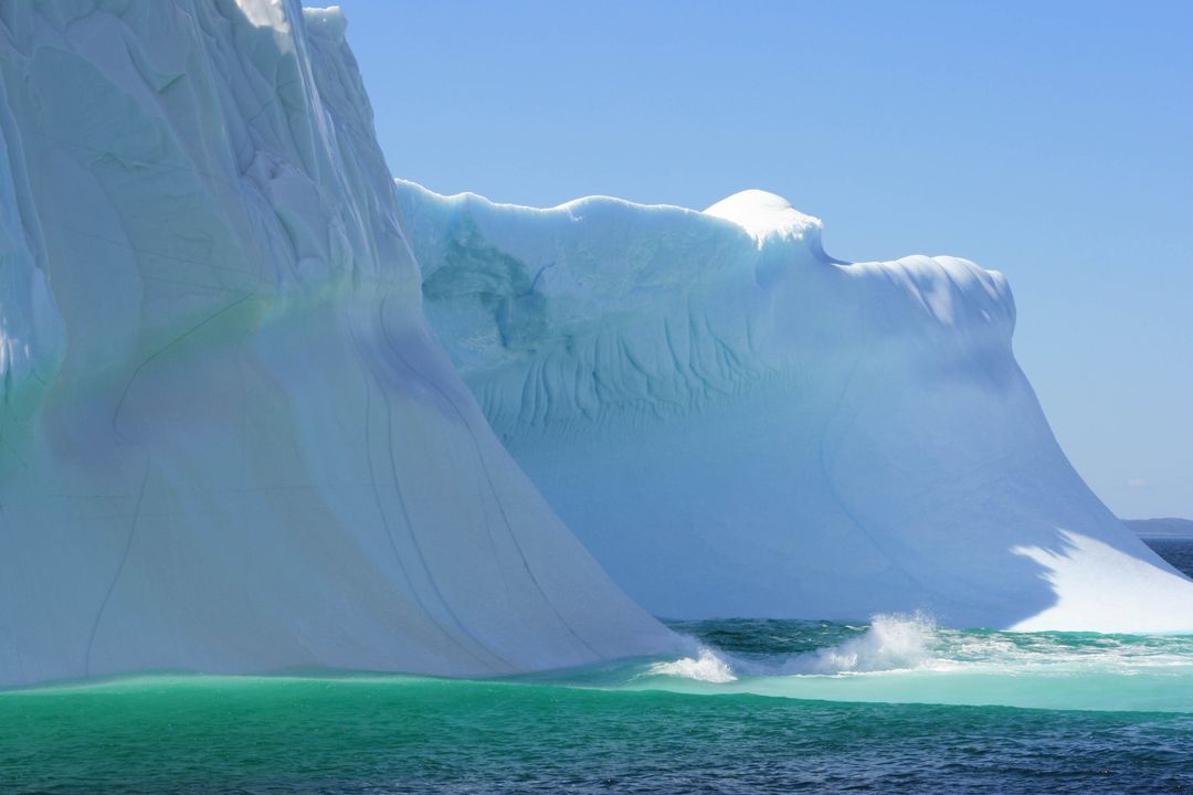 Towering Blue Iceberg Rising from Turquoise Ocean with Breaking Waves