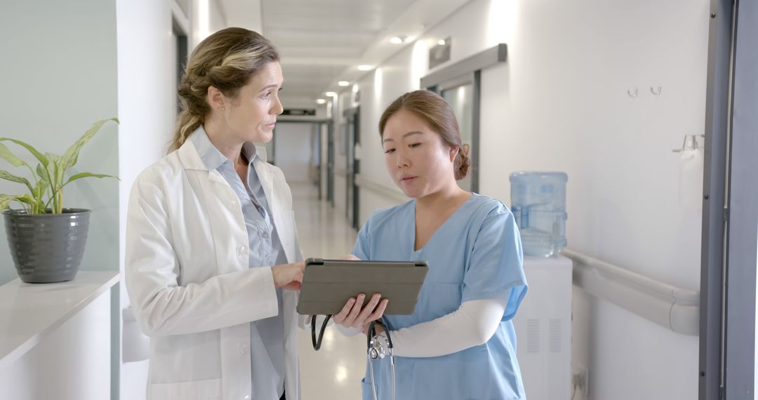 Medical Professionals Discussing Patient Data on Digital Tablet in Hospital Corridor - Free Images, Stock Photos and Pictures on Pikwizard.com