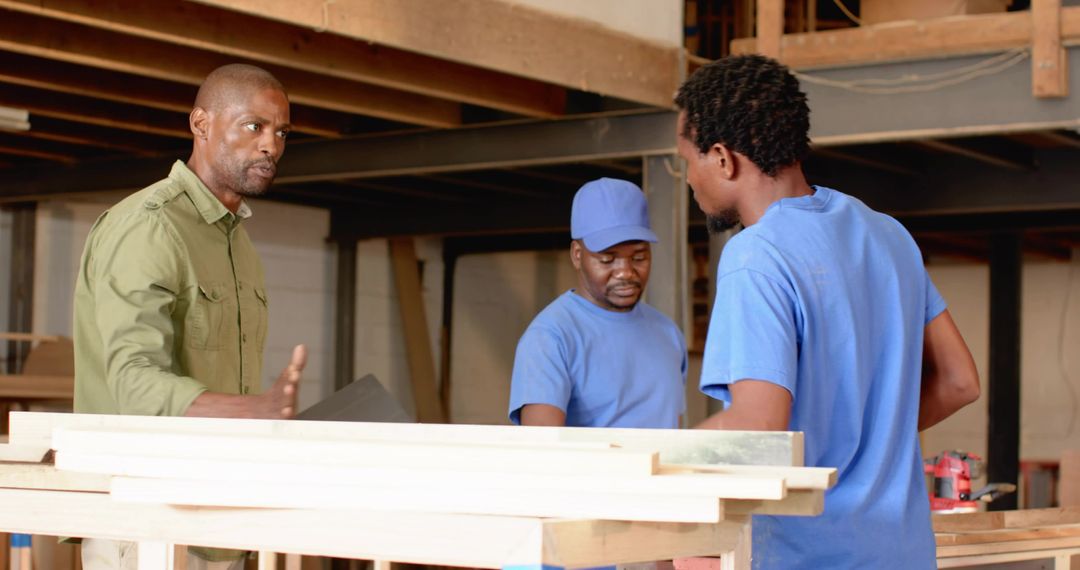 Foreman directing carpentry crew holding clipboard at wood workshop