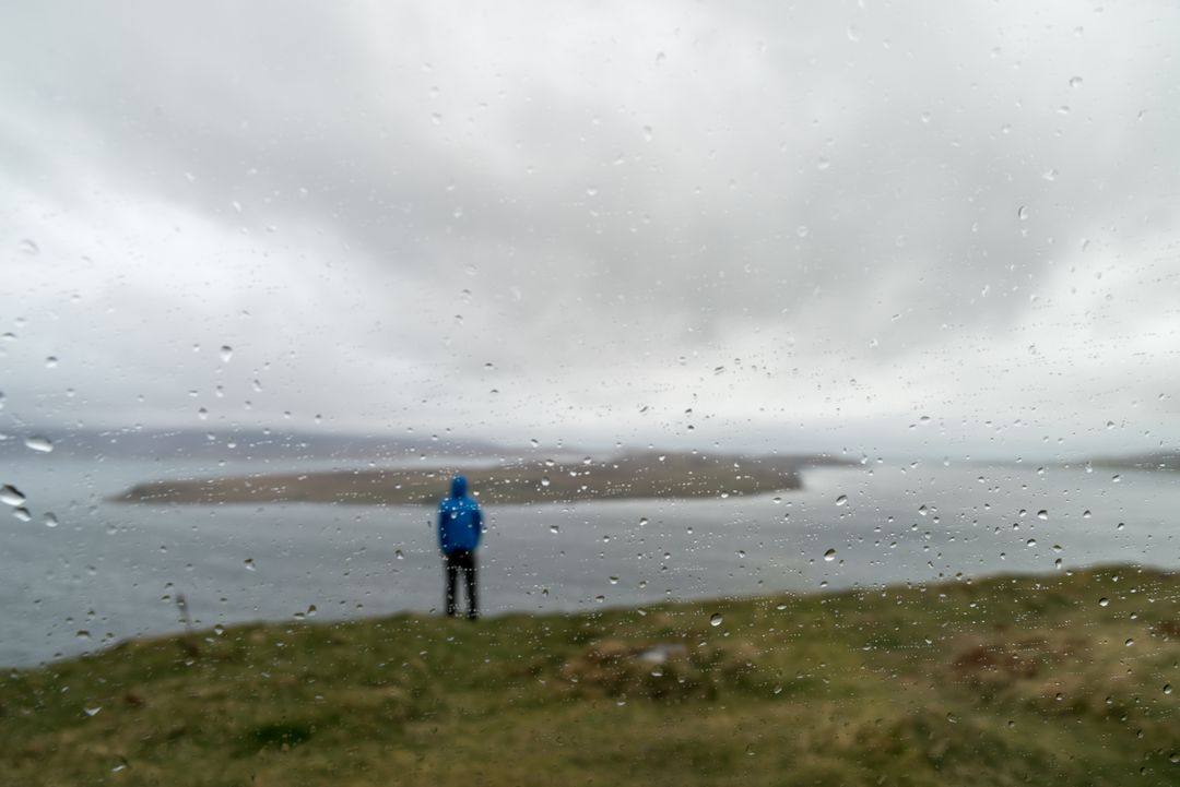 Person in Blue Raincoat Looking at Ocean on Overcast Day