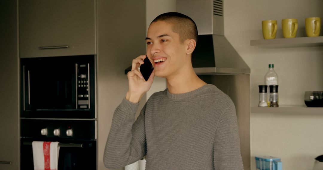 Young Man Smiling While Talking on Phone in Modern Kitchen - Free Images, Stock Photos and Pictures on Pikwizard.com